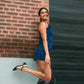 Woman in a blue dress standing against a brick wall